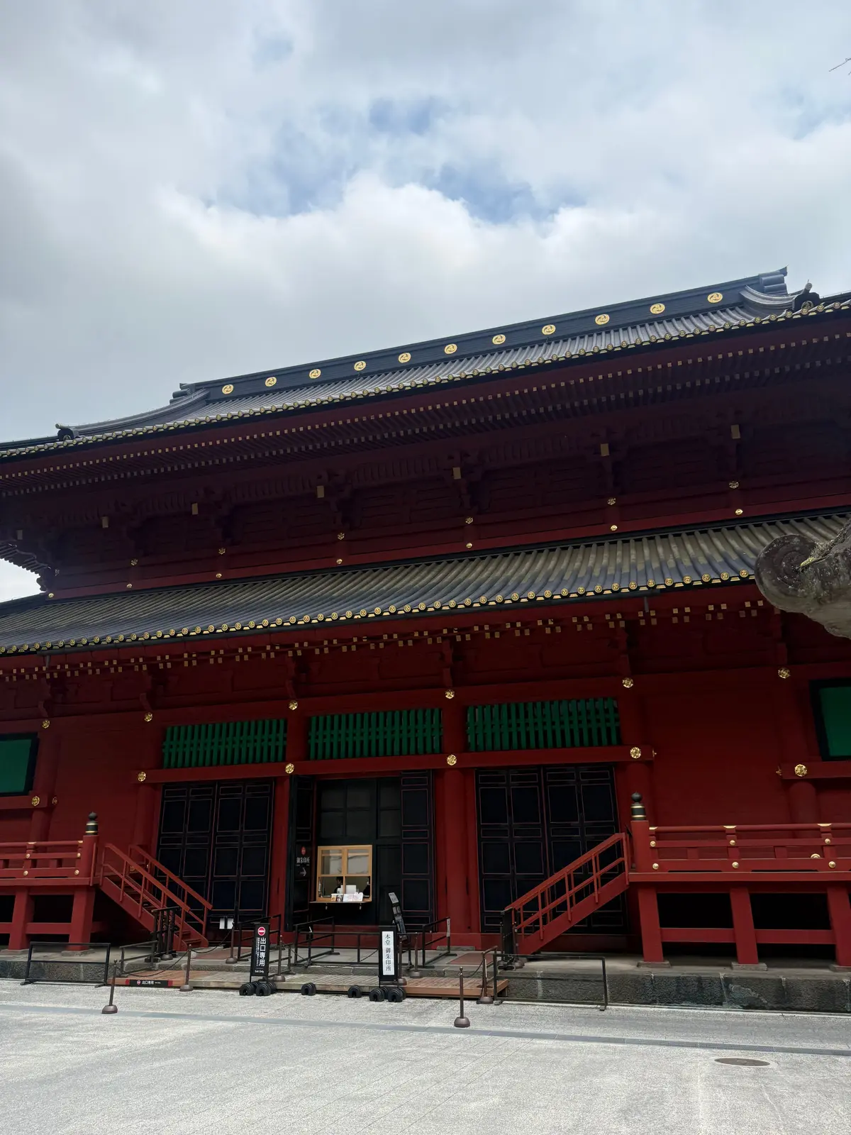 赤い伝統的な寺院の建物で、緑の窓と金色の装飾が施された屋根が特徴。両側に赤い階段が設置されている。