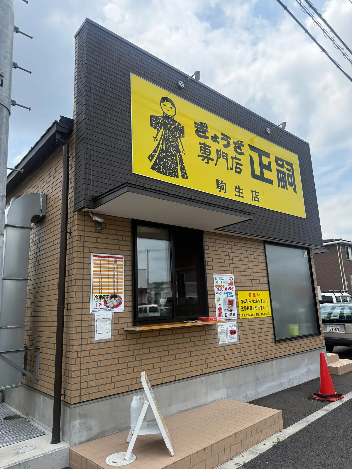 黄色の看板付きの鶏肉専門店 storefront、窓ガラスとレンガの壁、路上にはコーンが置かれている