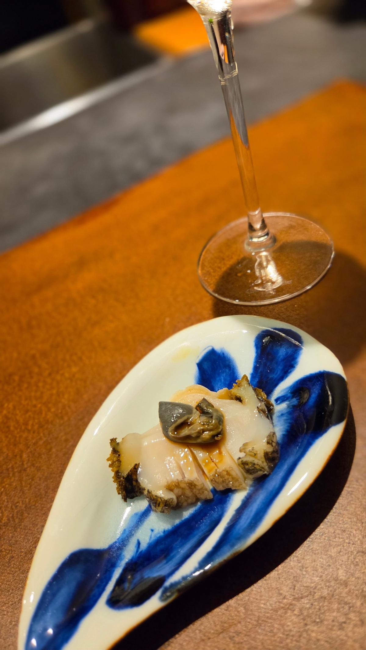 青と白の模様の皿に盛り付けられた、照り輝く光沢のある魚介料理。グラスに入った白ワインが隣に置かれている。