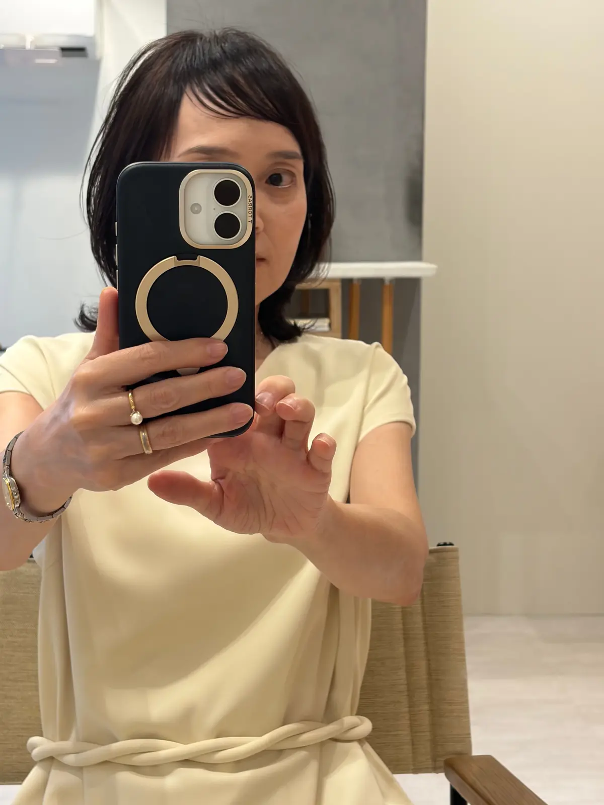 ベージュのトップスを着た女性が、スマートフォンで鏡の写真を撮影している。