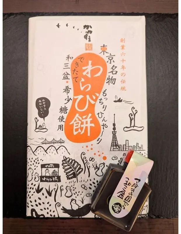 お土産の包装紙と小包が並ぶ。包装紙には「おたふく」の文字と東京タワーや山などのイラストが描かれている。