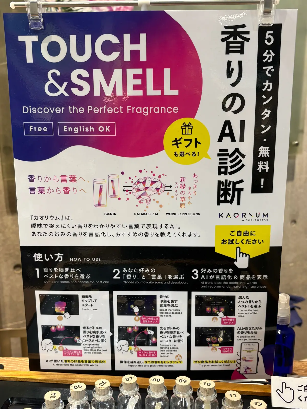 TOUCH & SMELLと書かれたパンフレット。紫と白の背景に、香りのAI診断を促す内容。手順が3つ表示され、香りボトルが並んでいる。