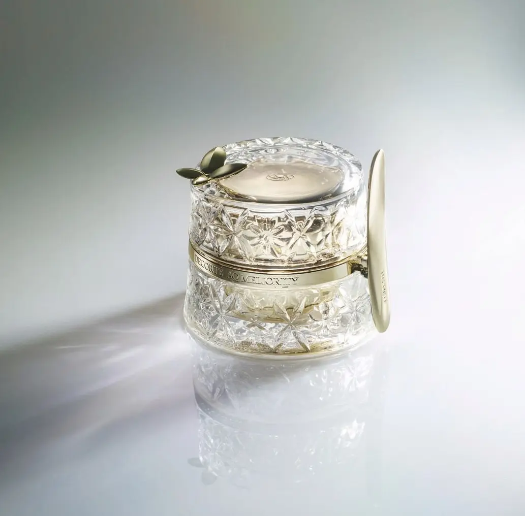 金色の縁取りとカットガラスの容器に入ったクリーム。上部には銀色の蓋、側面に「DECORTE AQ MELIOR」のロゴが刻印されている。白いスパチュラが添えられている。