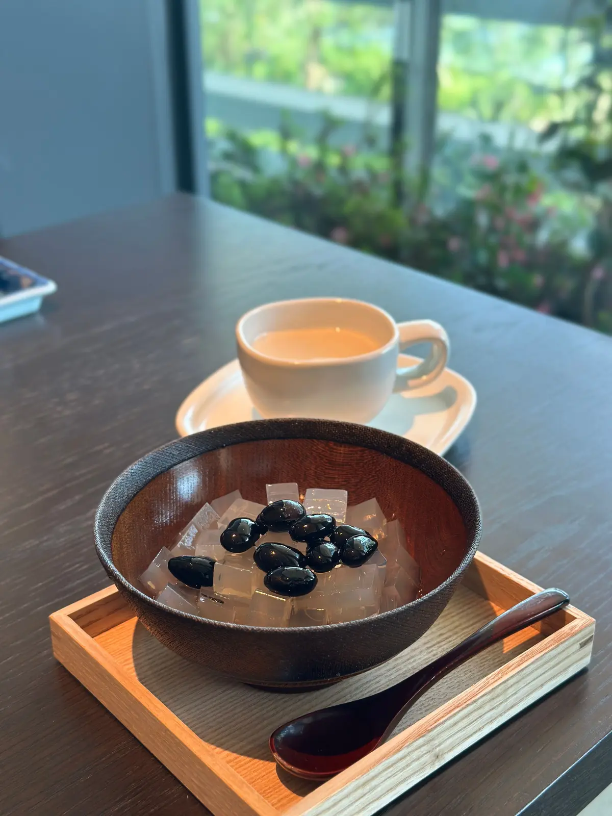 茶色の木製トレイに、氷と黒いオリーブが入った茶色のボウルと、茶色い液体が入った白いマグカップが置かれています。