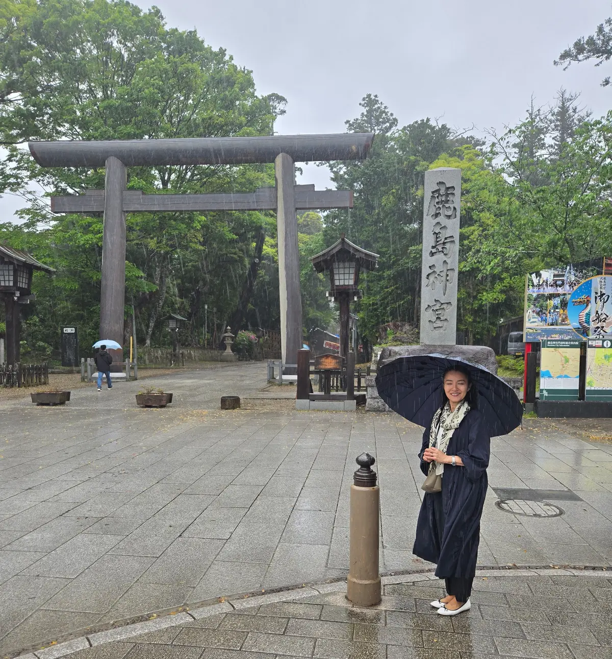 雨の中、石の鳥居を背景に女性が傘を差して立っている
