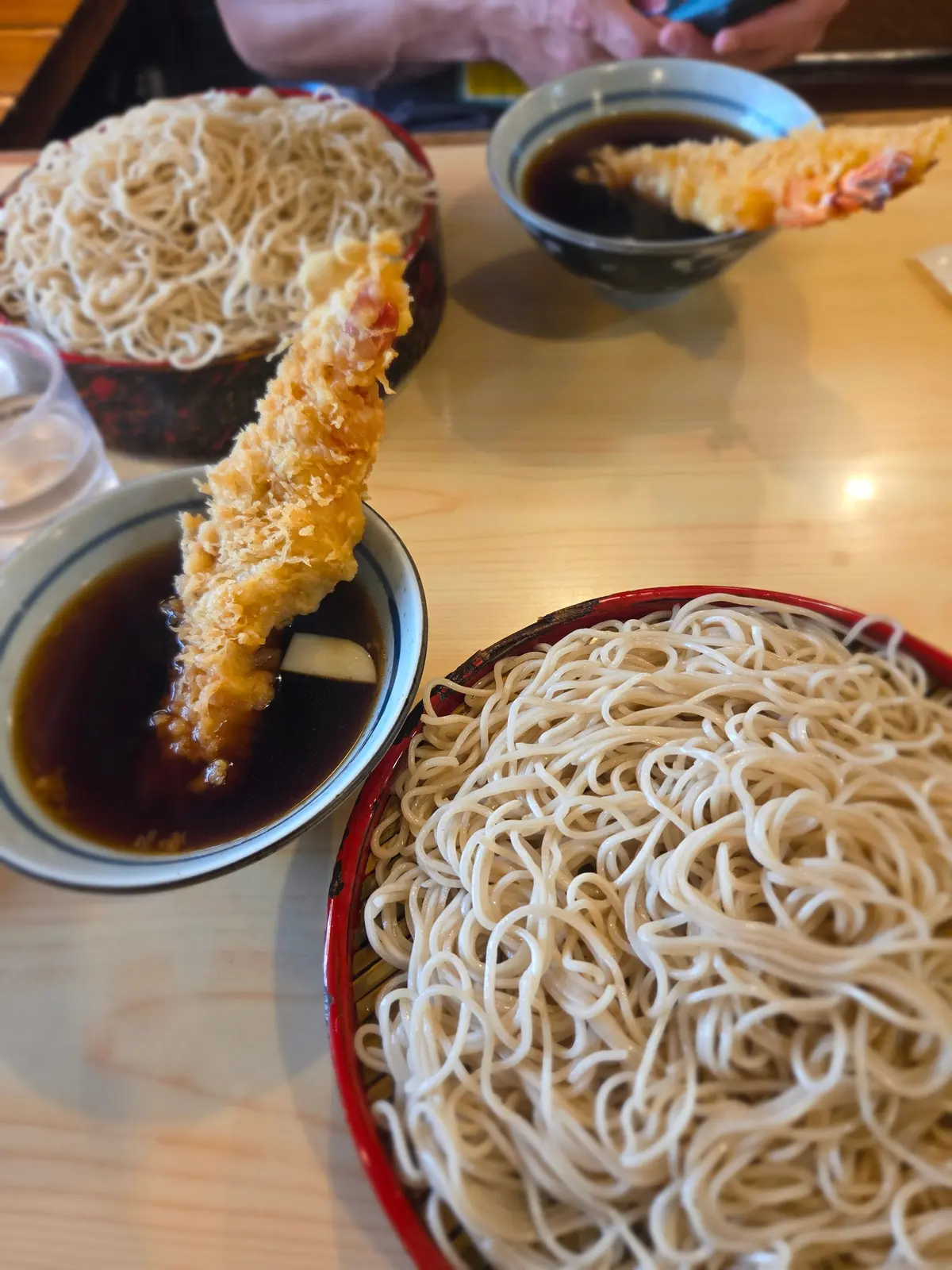 テーブルに置かれた、蕎麦とエビ天の料理。蕎麦は2つの漆器の皿に盛り付けられ、エビ天は小皿に添えられて醤油に浸っている。