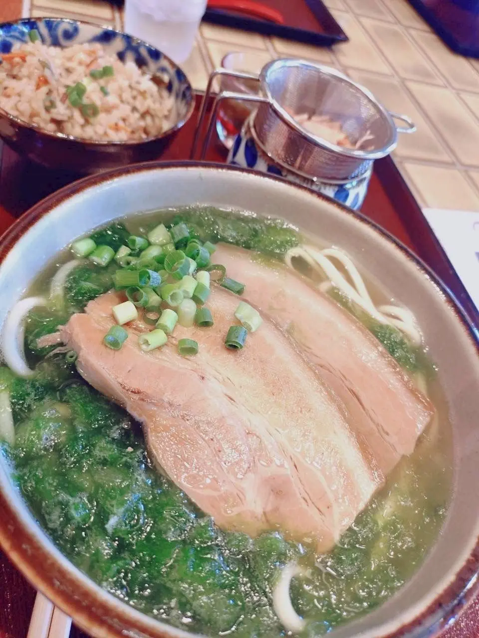 茶色の出汁にうどん、薄切りの鶏肉、ネギ、海苔が入ったうどん茶漬け。小皿に赤飯、茶漉しに茶葉も写っている。