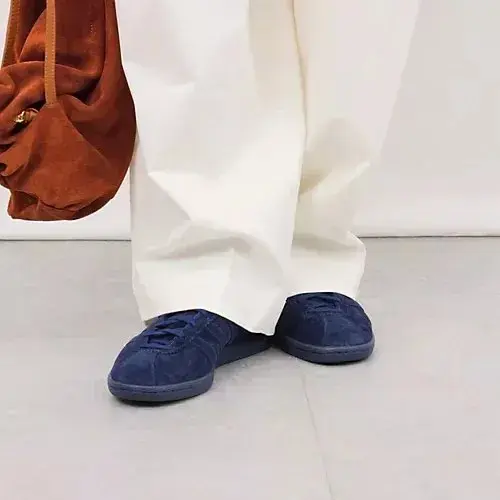 白のワイドパンツに、濃紺のスエード素材のAdidasサンバシューズを履いた足元。茶色の大きめのバッグを持つ。