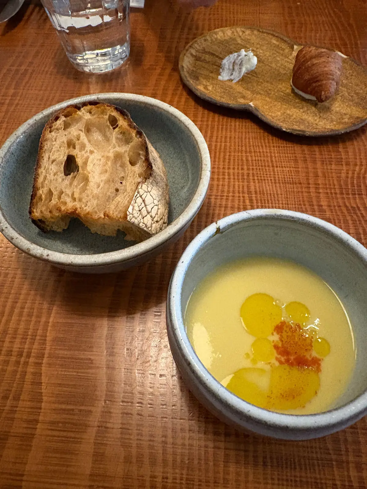 木製のテーブルに置かれた、3つの料理。左にはフォカッチャ、右奥にはバターとパン、手前には黄色いスープが入った器。それぞれが異なる陶器の皿に盛り付けられている。