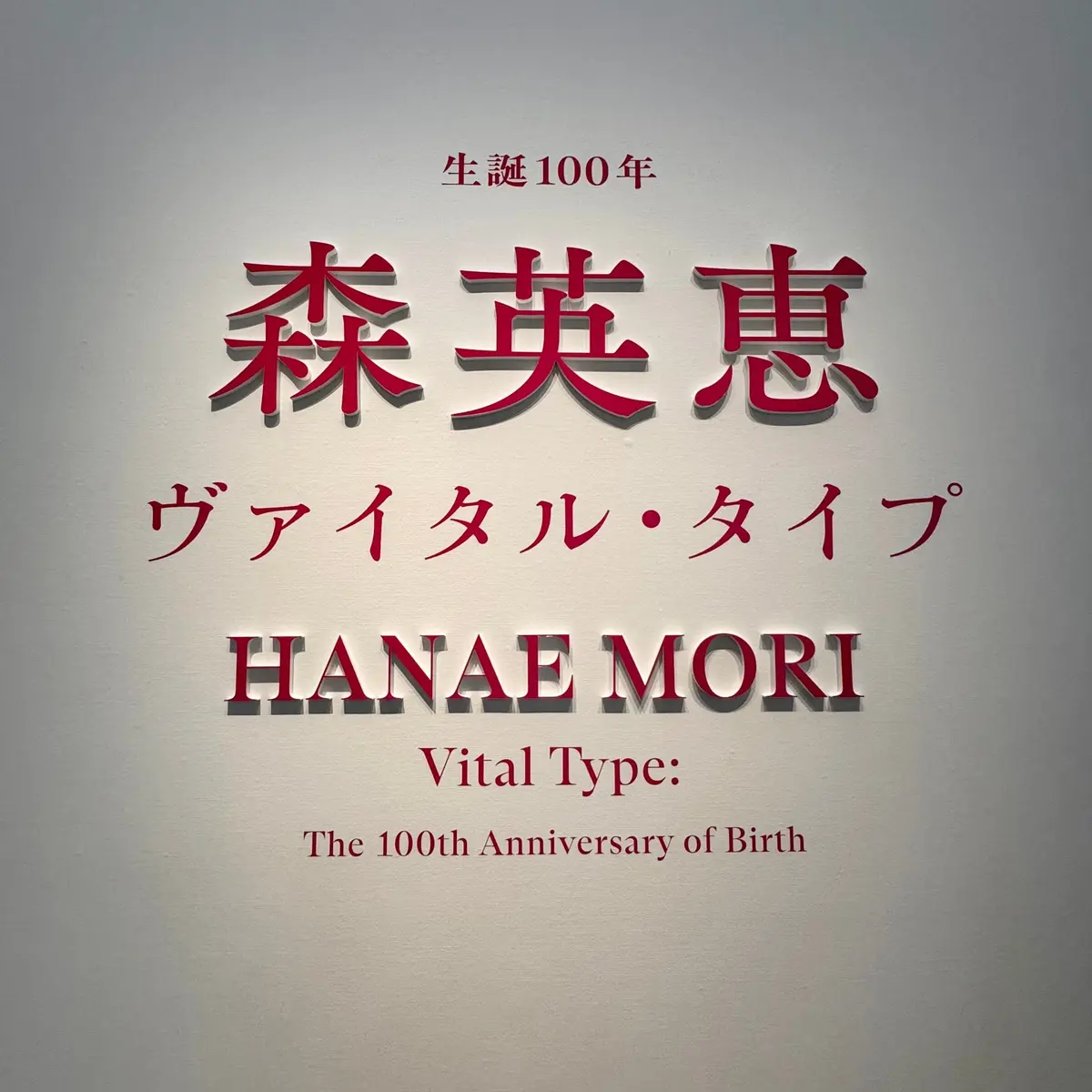 灰色の背景に、赤色の縁取りで書かれた日本語と英語のテキスト。「森英恵」と「HANAE MORI」のタイトル、および「Vital Type」の文字が配置されている。上部には「生誕100年」と記載。