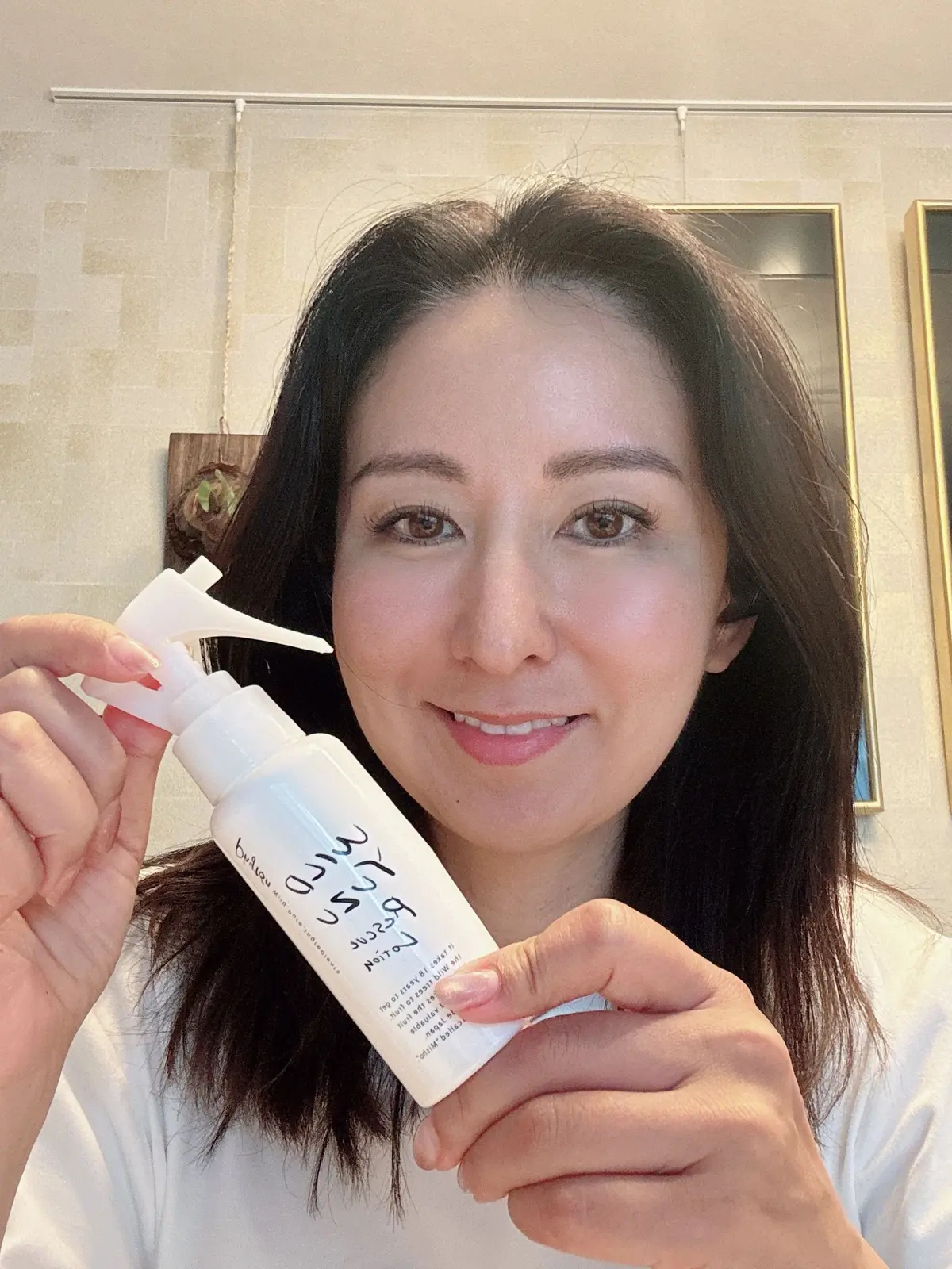 女性が白いボトルを持った手で、ミルクボリュームのヘアケア製品を提示している。ボトルには「ミルクボリューム」と記載され、背景には淡い色の壁と装飾品が見える。
