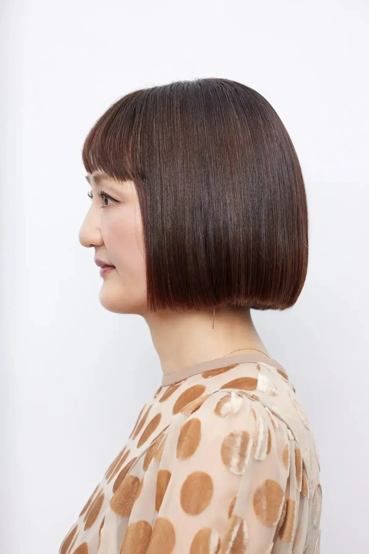 ショートボブの女性が横顔で、茶色の髪が耳より長く、淡いピンクのドット柄の服を着ている