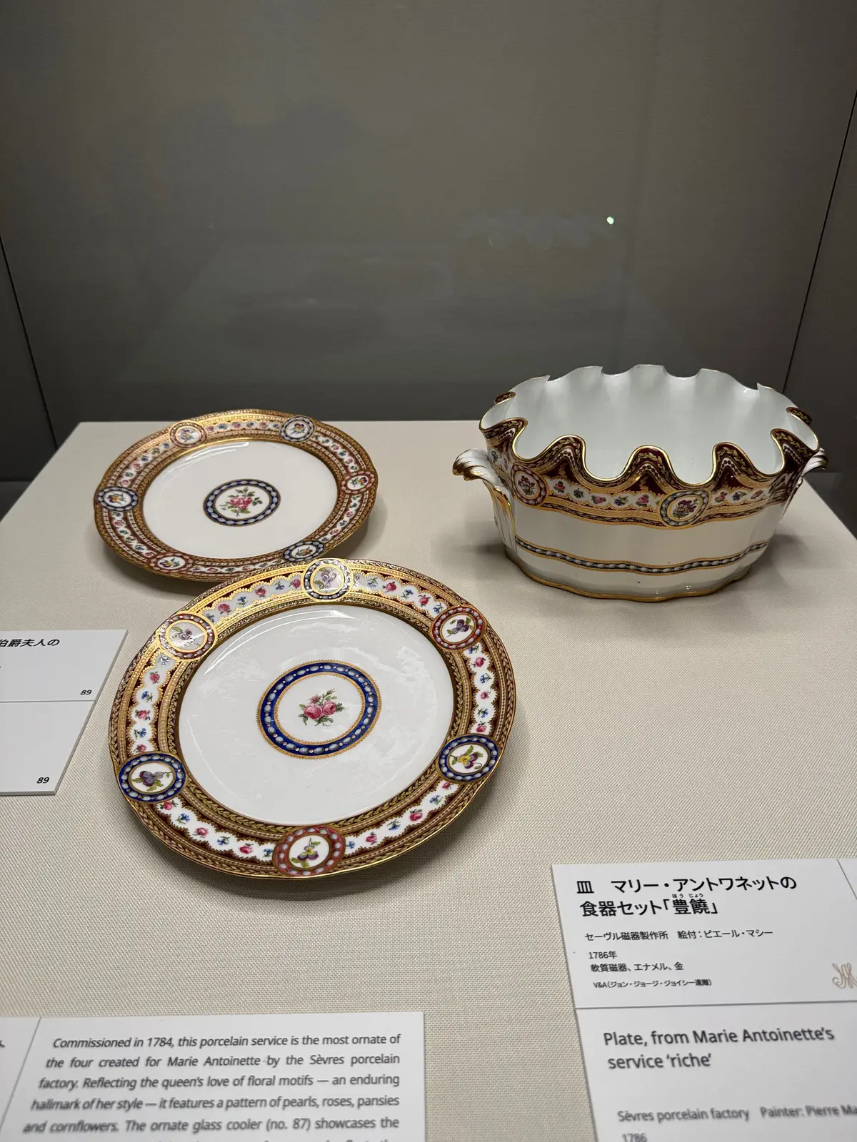 白地に金彩と多彩な花模様が描かれた、マリー・アントワネットの食器セット。平皿2枚と、フタ付きのガラス製クーラーが展示されている。