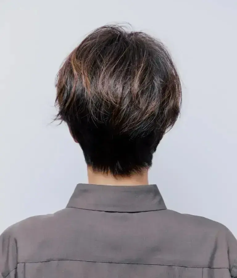 後ろから見たショートカットの女性。髪は黒と茶色で、グレーのシャツを着ている。