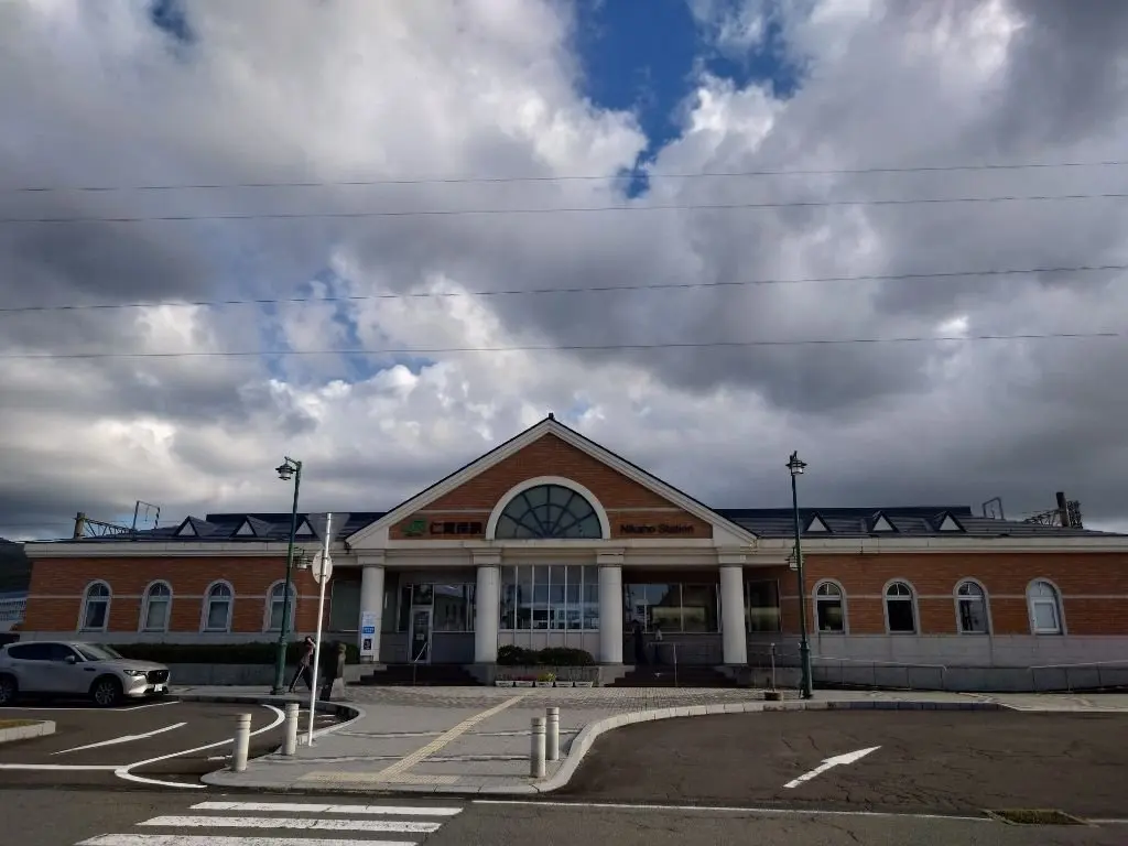 日本の中央線にある、赤レンガのNikaho駅舎。アーチ型の入り口が特徴で、曇り空の下に建っている。駅の標識が日本語と英語で表示されている。