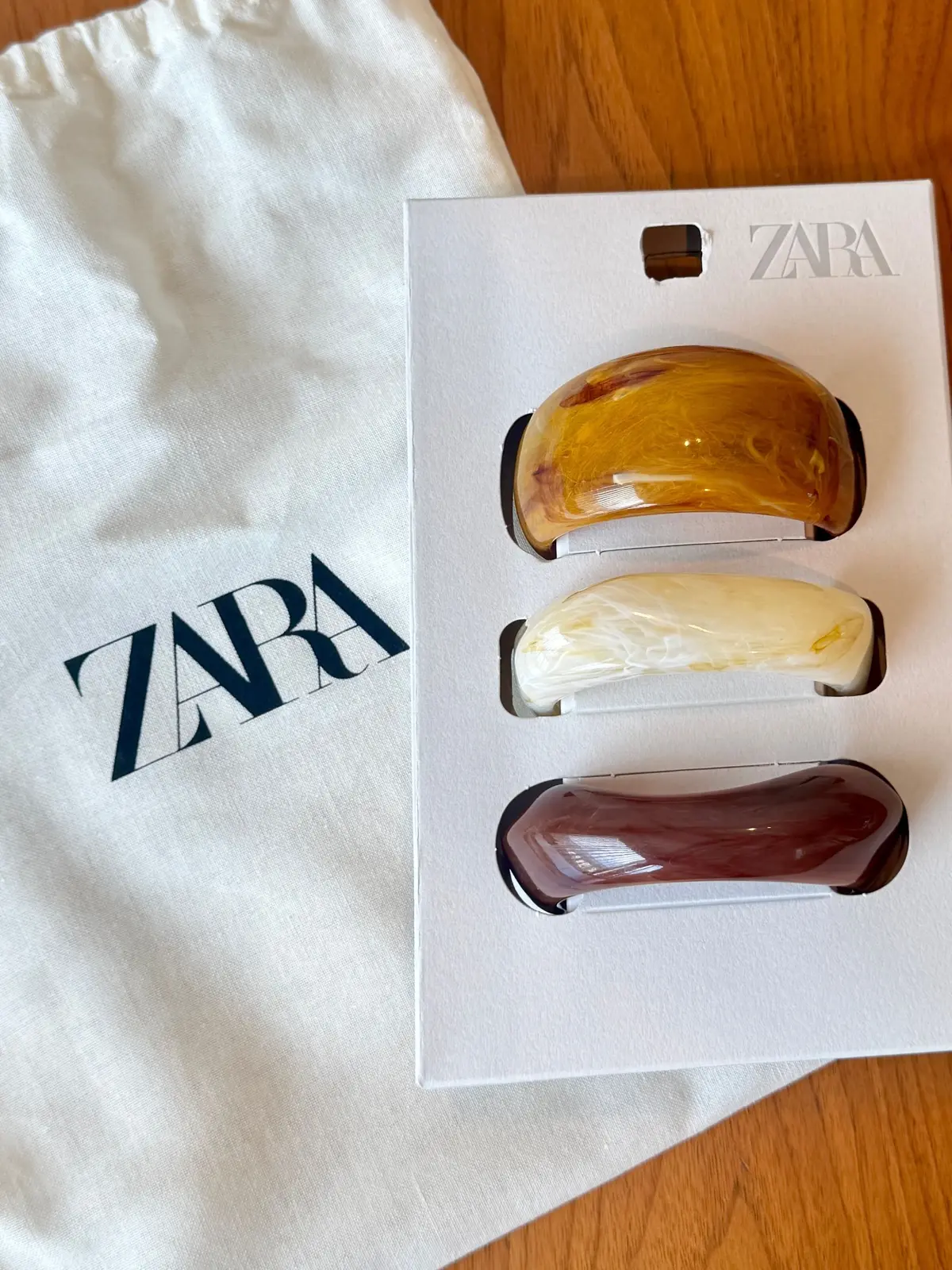 ZARAの3点セット。琥珀色、オフホワイト、濃い赤茶色の樹脂製ハンドル3つが箱に並んでいる。白い布製のバッグが隣に置かれている。
