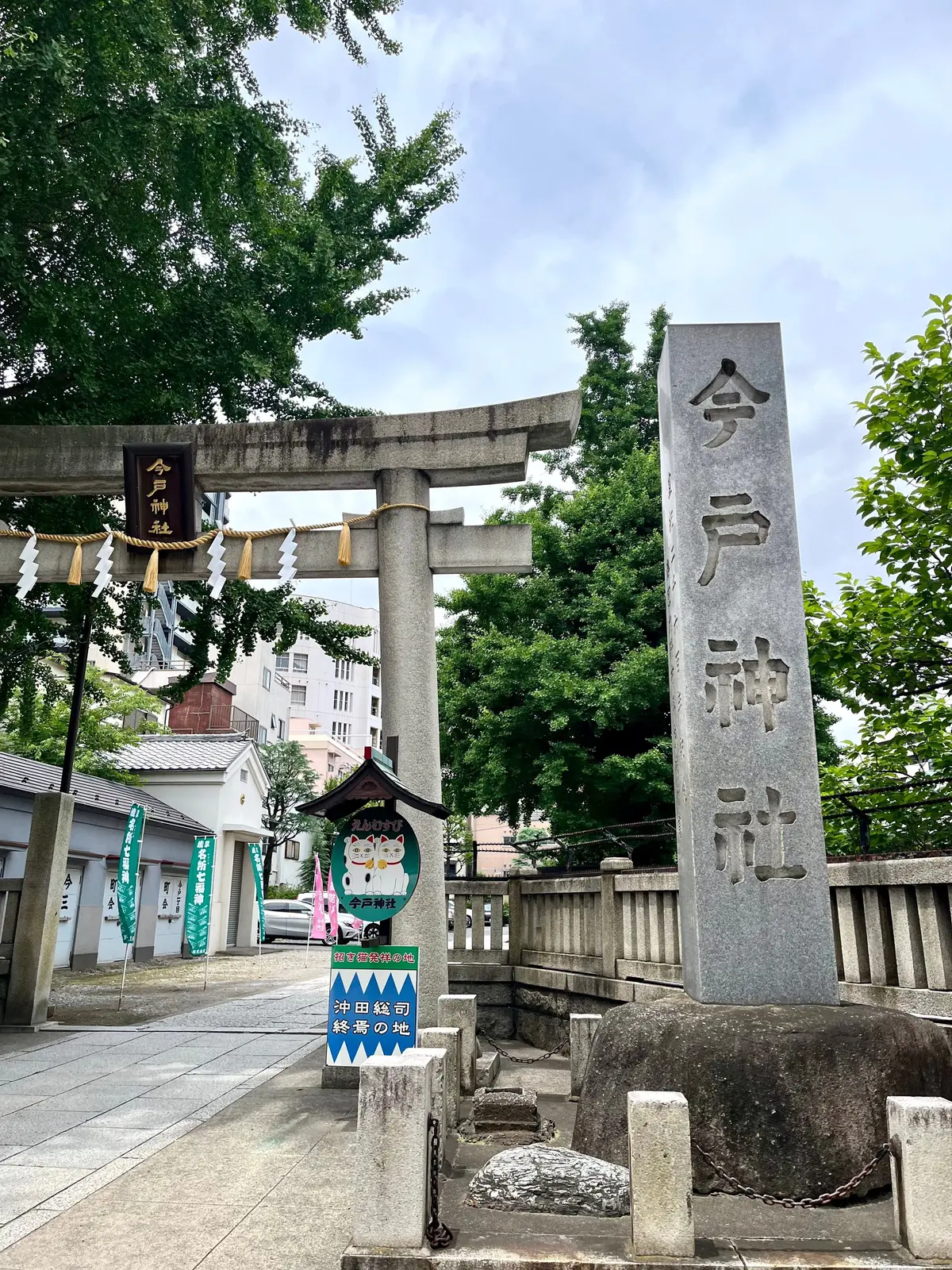 石碑と鳥居のある神社。鳥居は木製で、屋根は瓦。石碑には漢字で「今戸神社」と書かれている。背景には住宅街と緑豊かな木々が見える。