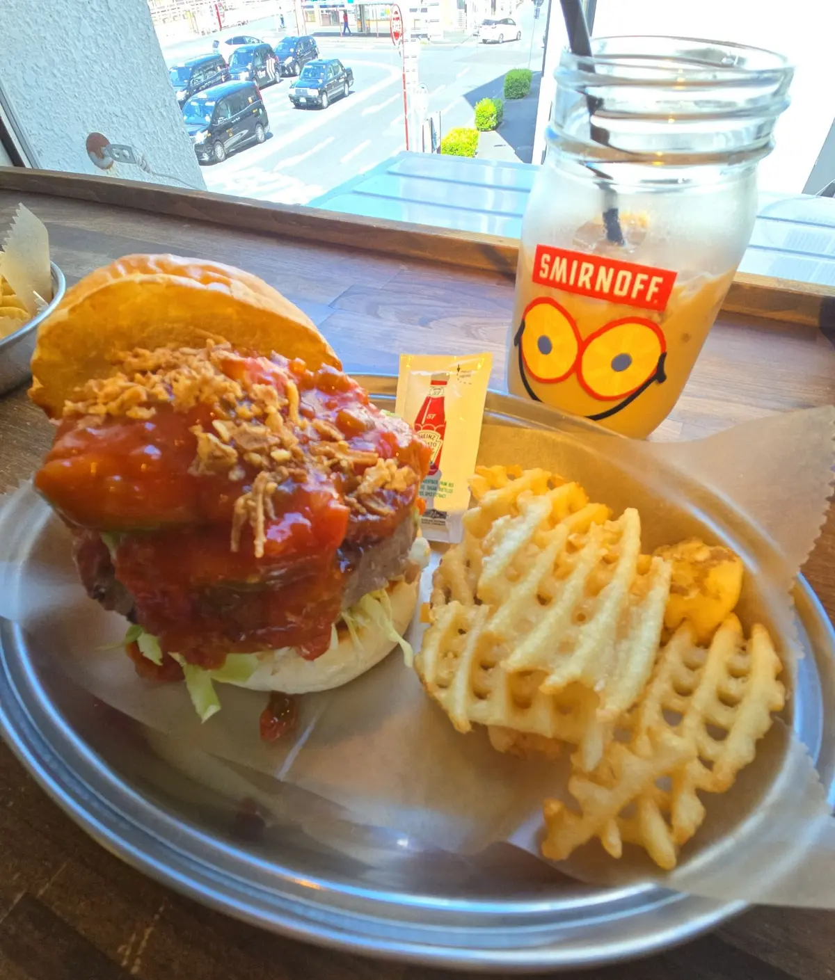 ハンバーガーとワッフルポテトが盛り付けられたプレートで、背景にはスマイノフのグラスが置かれている