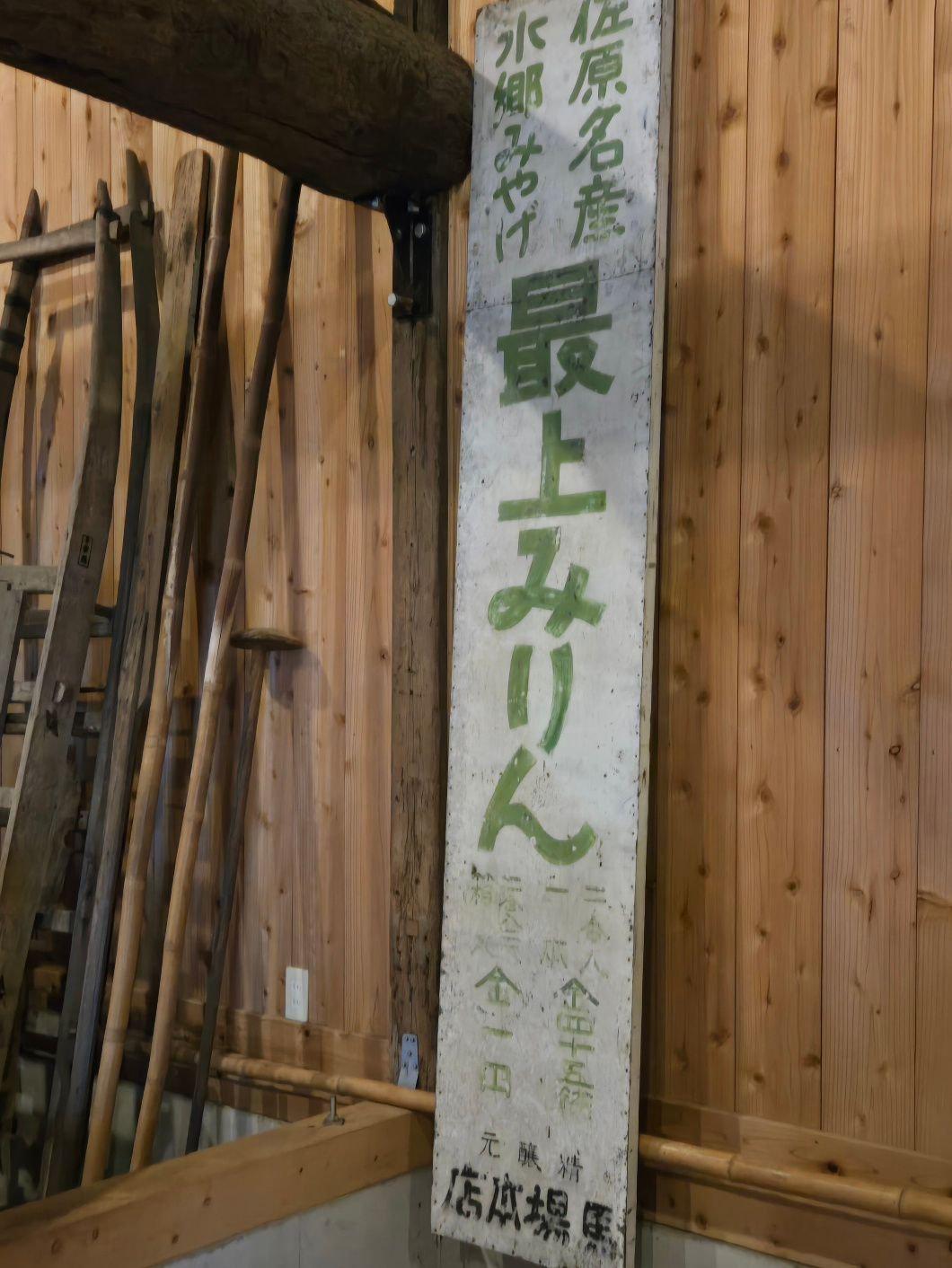 木製の壁に緑の文字で書かれた看板「上之台二丁目」が立てられ、横に木製の道具が並んでいる