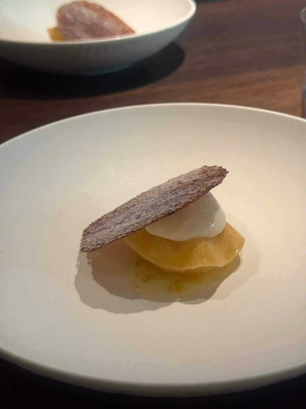 白い皿に盛り付けられたデザート。梨のコンポートの上に、チョコレートのクランブルが乗せられている。背景には同じデザートが別の皿に置かれている。