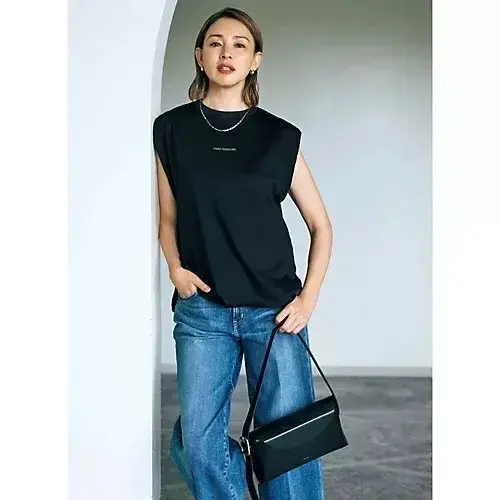 黒い肩なしTシャツにデニムを合わせた女性。正面から見下ろすアングルで、右手に黒いショルダーバッグを持ち、左手はポケットに。シンプルなネックレスを着用し、背景には白いアーチ型空間。