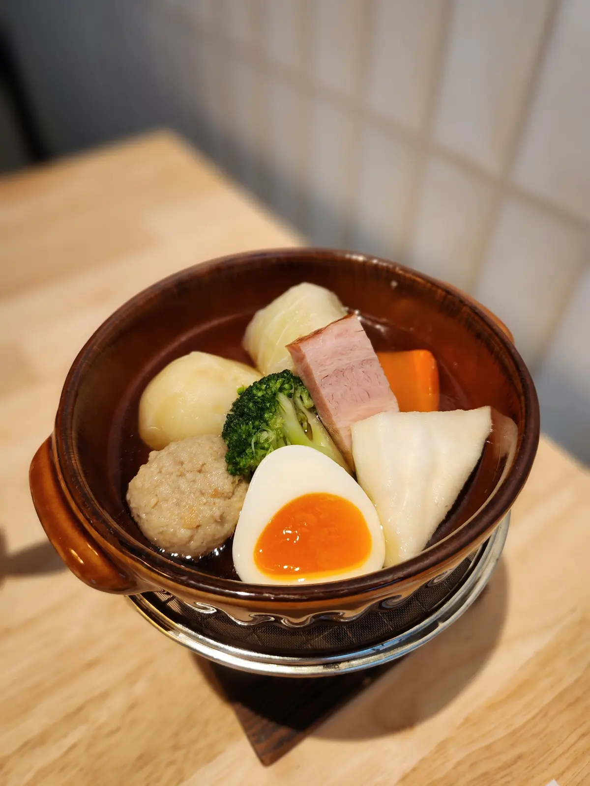 茶色の陶器鉢に盛り付けられた、半熟卵、肉、野菜の煮物。ポテト、ブロッコリー、キャベツ、人参など、様々な食材が彩り豊かに並んでいる。