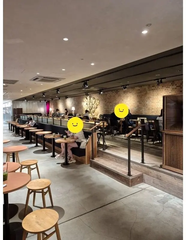スターバックス店舗の内部。木目調のテーブルと椅子が並び、右壁にはレンガとアート作品が配置されている。数名が席で休憩している。