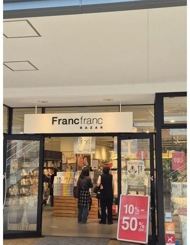 Francfrancバザール店舗の入り口。自動ドアがあり、店内には雑貨が並んでいる。入り口付近にはセール告知の立て看板が置かれている。