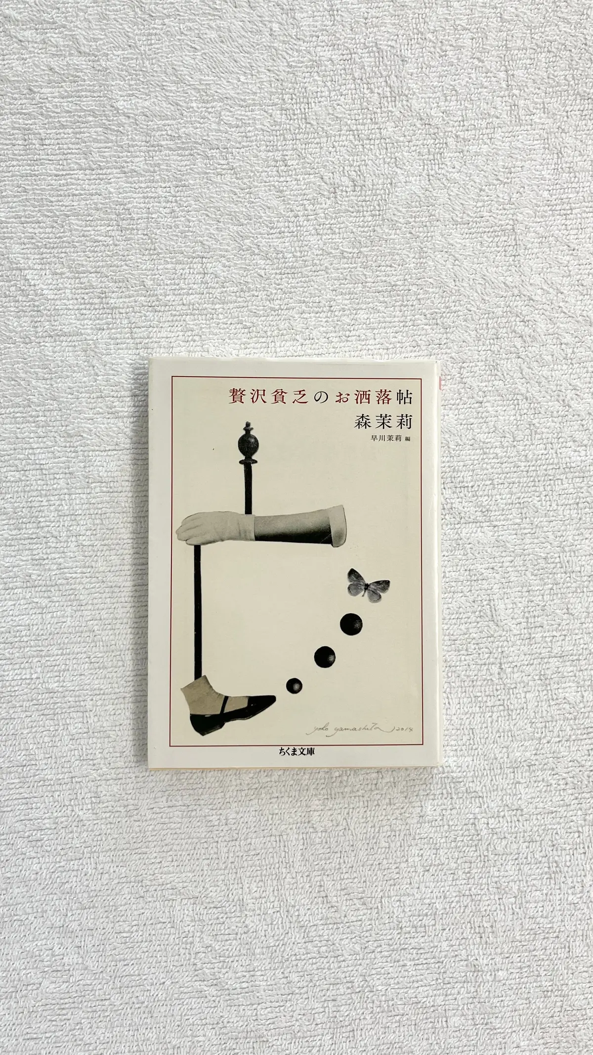 背景の白い壁に置かれた、イラストが描かれた本の表紙。
タイトルは「贅沢貧乏」、作者は「森栄莉」とある。
イラストは、手袋をはめた手がワイングラスを持ち、蝶が舞う様子。
下部に「ふくま文庫」のロゴが見える。
