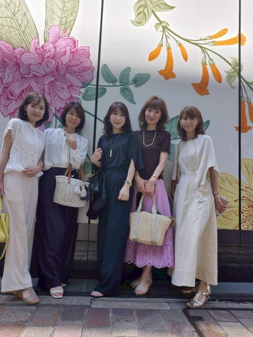 白シャツを着た2人の女性が、マーブル模様のテーブルを挟んで座り、それぞれバースデーデザートの入った白い皿を見つめている。背景には高層ビルの窓が見える。