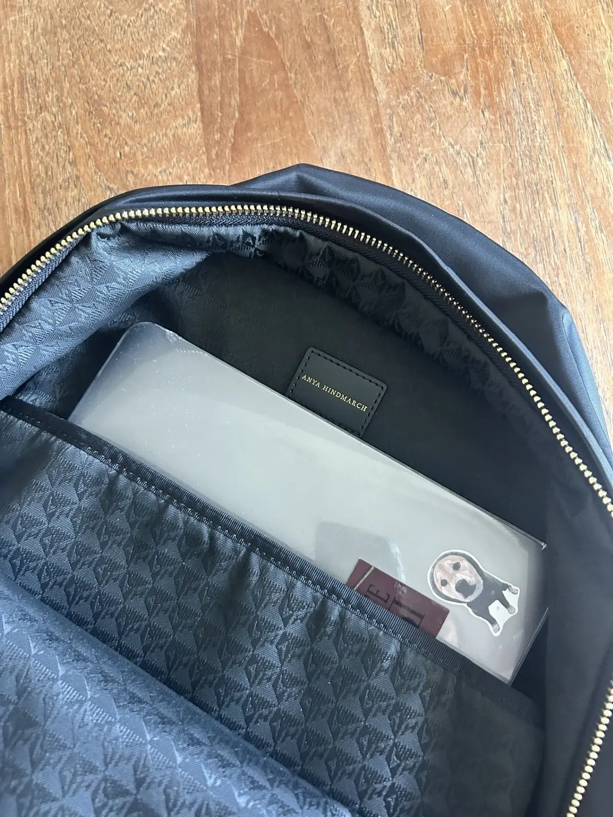 黒いリュックの内側の様子。グレーの布地に「ANYA HINDMARCH」のロゴが入ったタグと、赤い背景に白黒のイラストがプリントされたカードが挿入されている。内側は全体的にグレーの布地で覆われている。