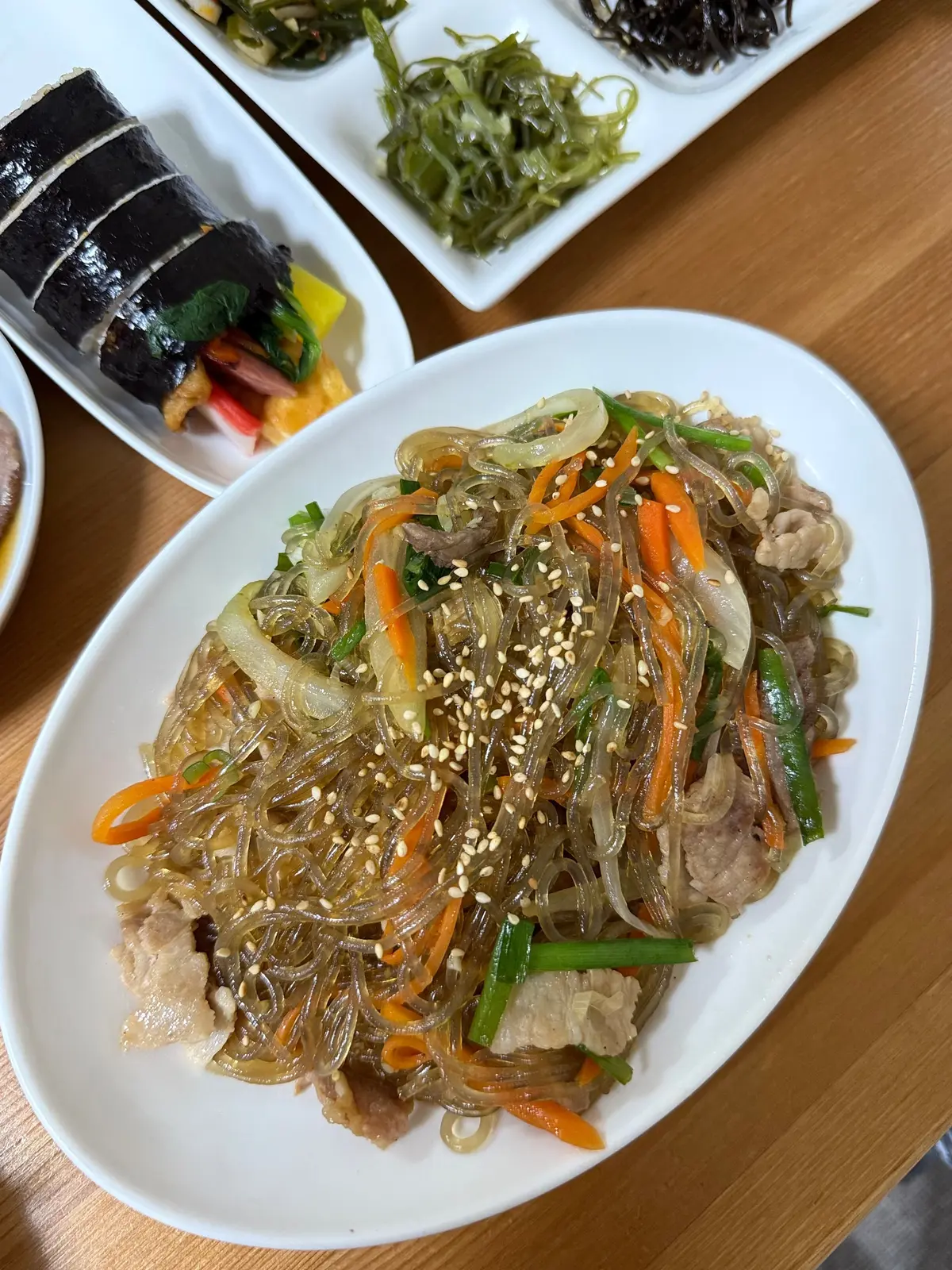 韓国料理 釜山 予約が取れないお店　尼崎グルメ　チャプチェ　白い楕円形の皿に、細い透明な麺と鶏肉、にんじん、ねぎがトッピングされ、ごま粒が散りばめられた料理。