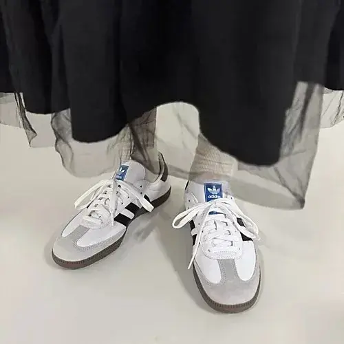 白いスニーカーを履いた足元。アディダスのロゴが青と白で入っている。スカートの裾がふんわりと広がっている。