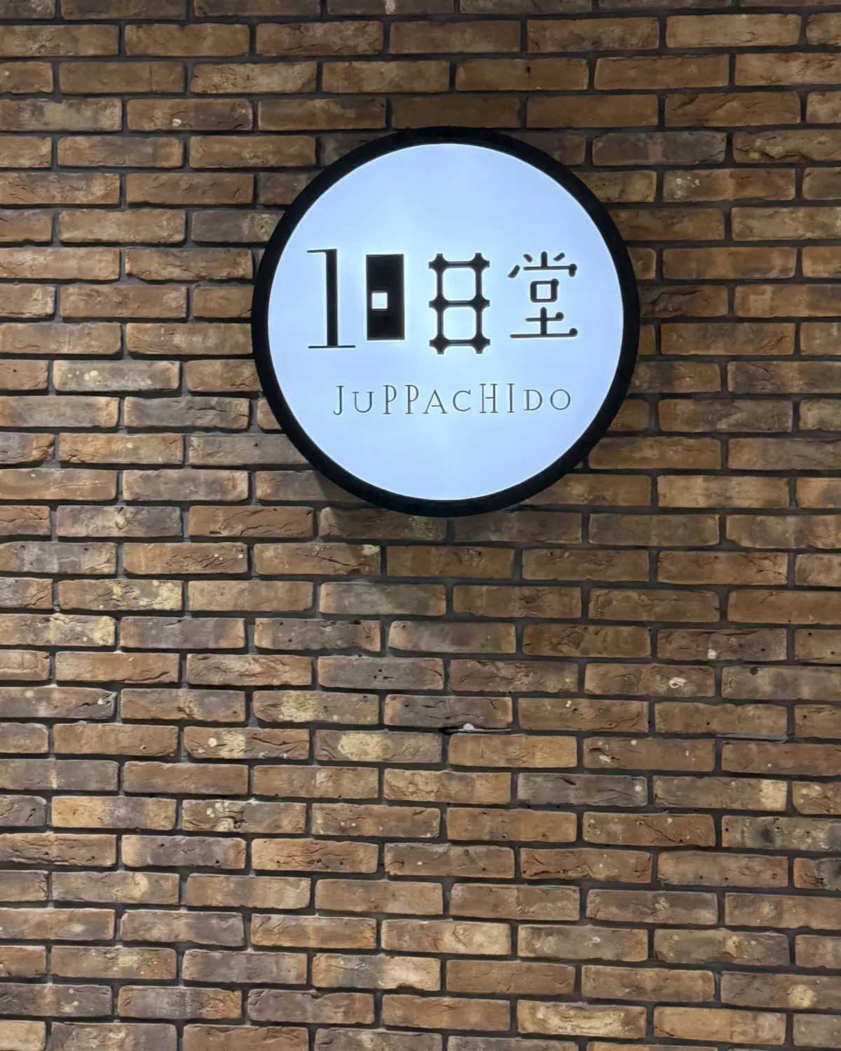 レンガの壁に設置された、黒い円形のネオンサイン。中央に「10日堂」の文字と、その下に英語で「JUPPACHIDO」と表記されている。