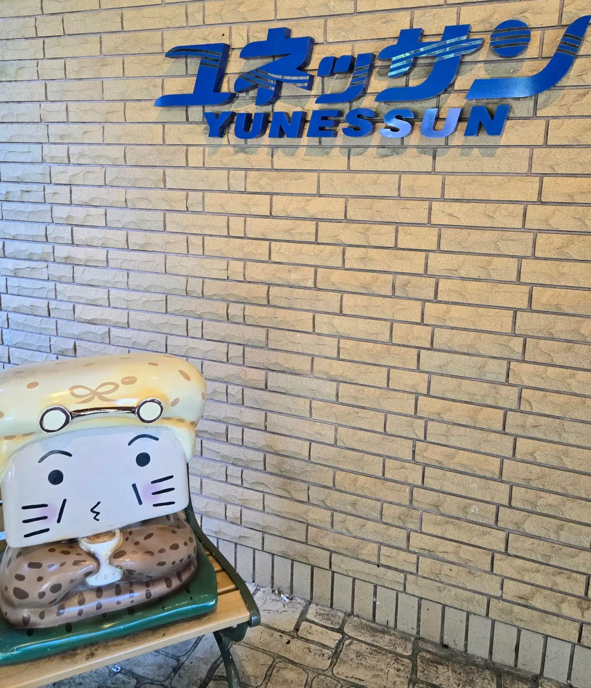 背景には、レンガの壁に青い文字でユネッサンと書かれた看板がある。