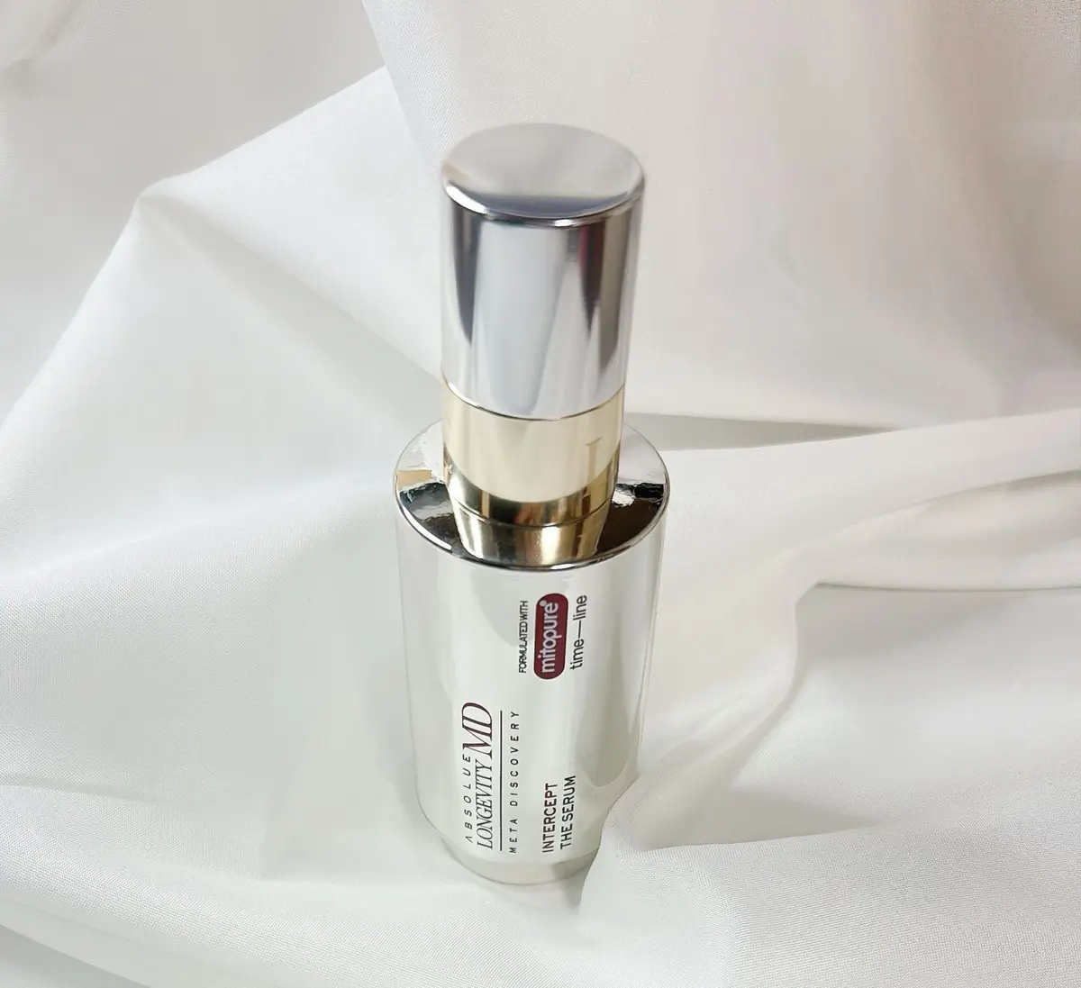 白い台紙の上に置かれた、長方形の白い化粧品ボトル。ラベルには「ABSOLUE LONGEVITY MD INTERCEPT THE SERUM」の文字と、赤いラインが入った「mitopure time-line」のロゴが記載されている。