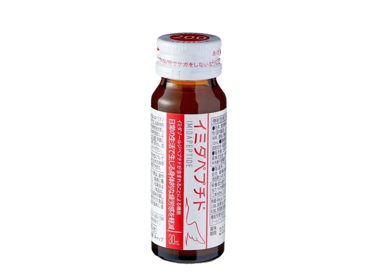 茶色の液体が入った、イムダペプチドという記載のあるペットボトル飲料。右側に日本語のラベルが貼られている。背景は明るいベージュ色。