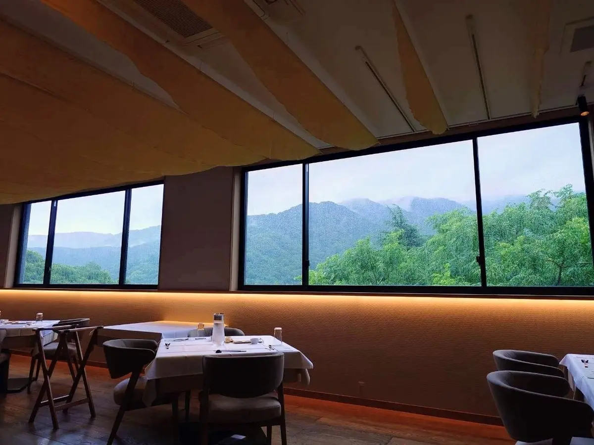 三輪湯河原のレストランのテーブル席と、窓の外に広がる緑豊かな山々。
