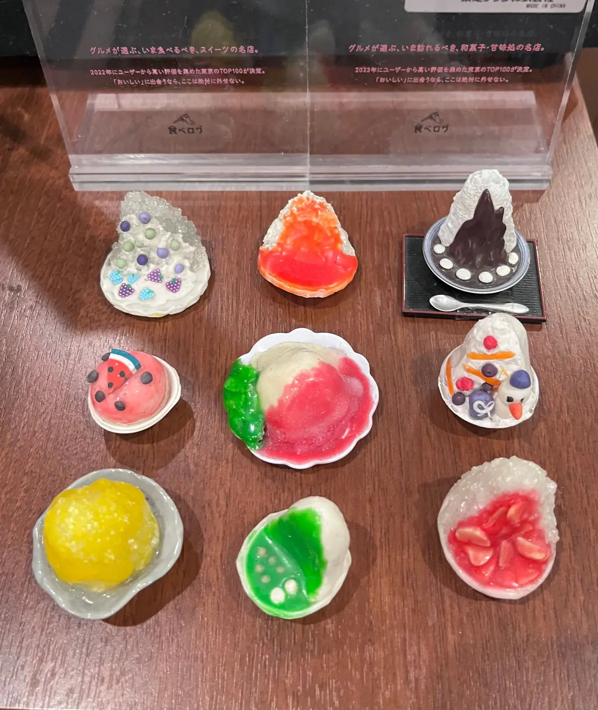 ベトロの「スイーツな気分」シリーズのミニチュア菓子コレクション。様々な色と形の可愛らしいお菓子が、黒い台座に固定され、背景には説明文とベトロのロゴが入ったカードが置かれている。