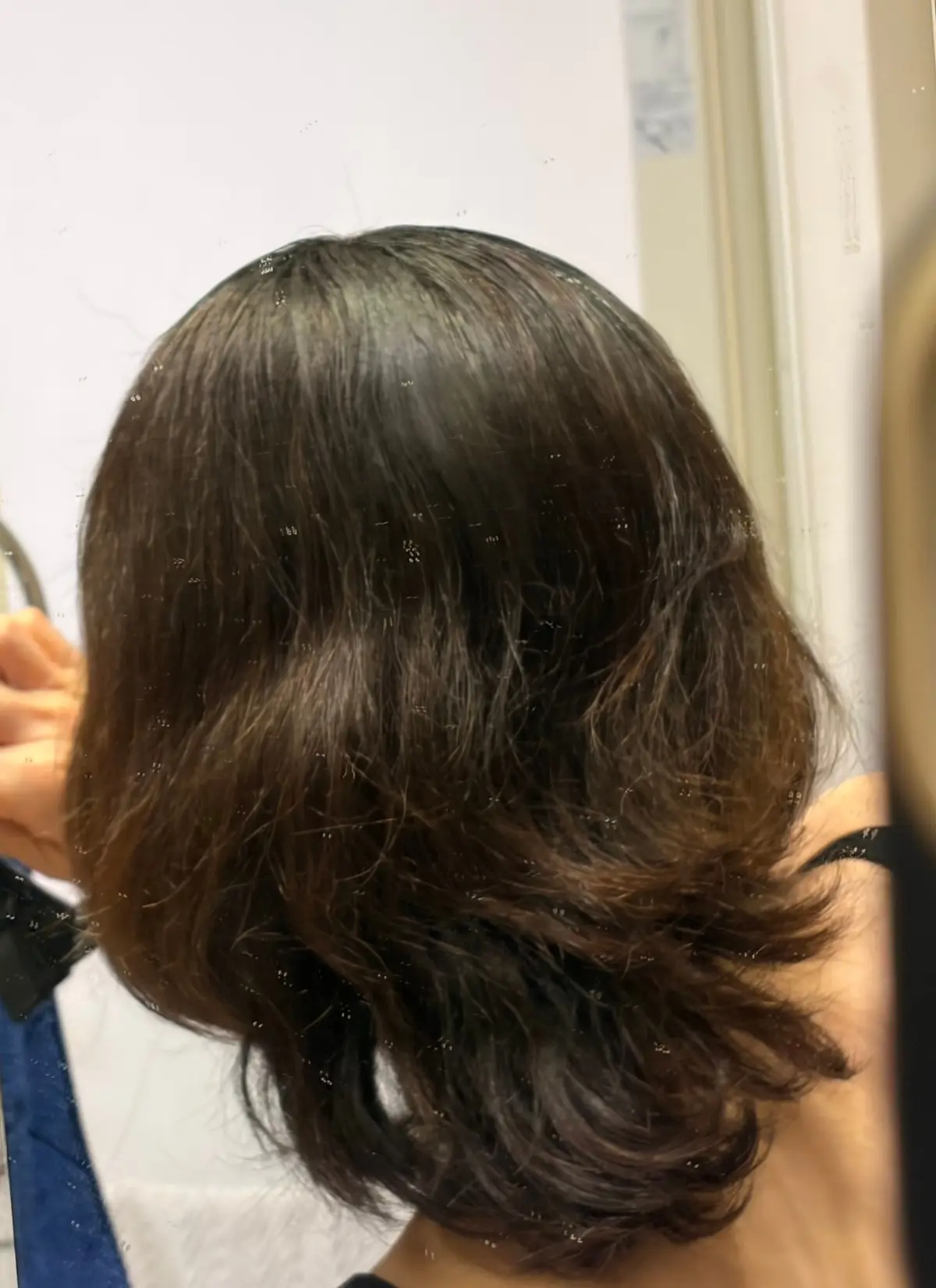茶色のボブヘアが、鏡に映っている。右側はスタイリングされ、左側は自然な状態。 Dysonのヘアードライヤーが写っている。
