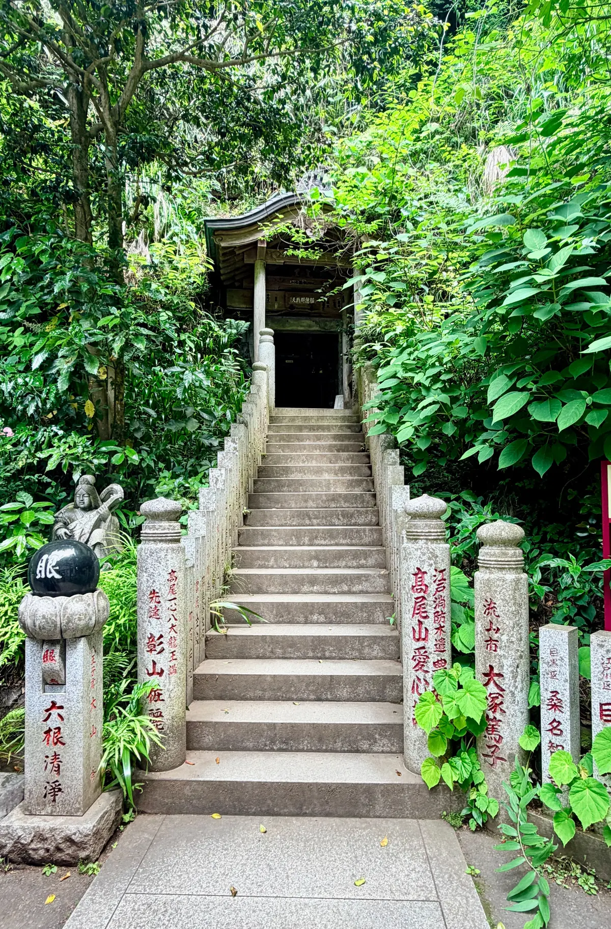 緑豊かな森の中、石段を登る参道。左右に石柱と石碑が立ち、奥に小さな社殿が見える。