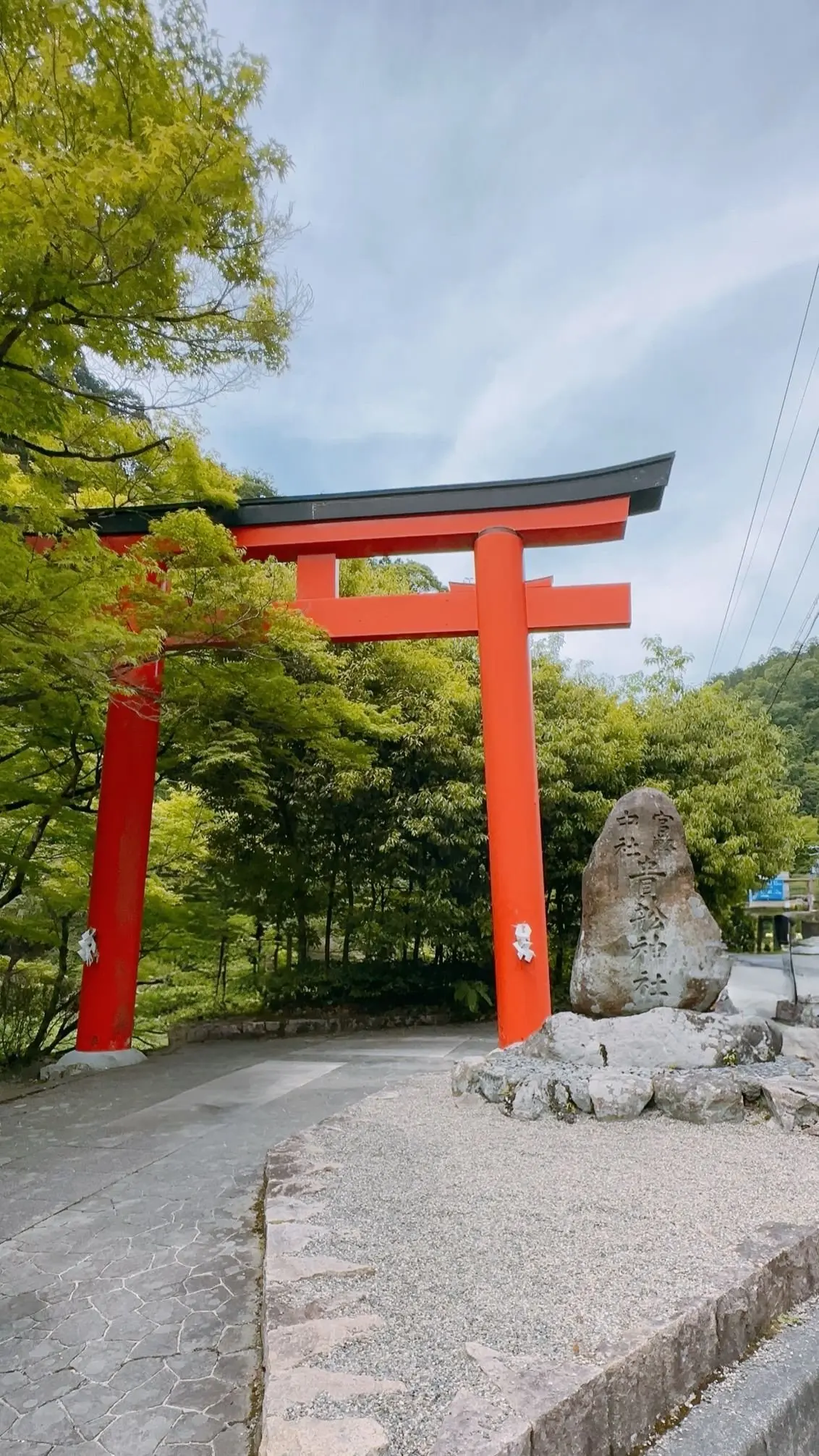 赤い鳥居が緑豊かな木々の中で立ち、石の碑が隣接しています。