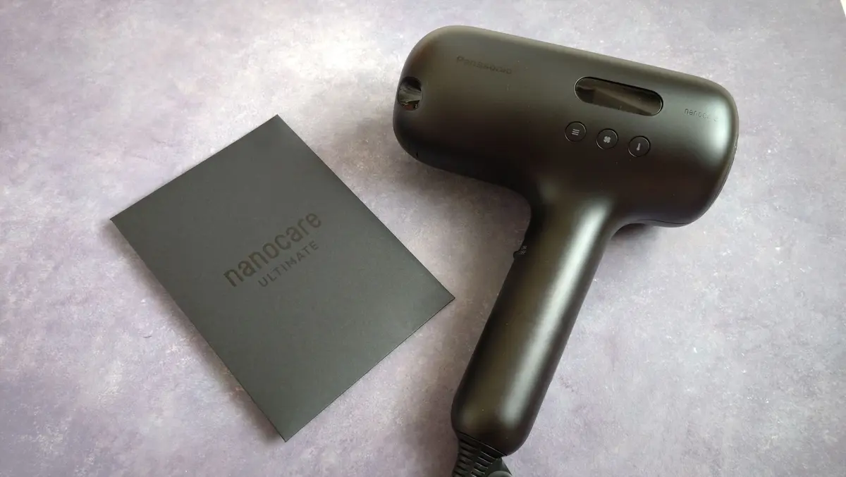 紫色の背景に置かれたパナソニックのナノケア Ultimate ヘアードライヤー。黒い収納ケースが左にあり、ドライヤーは右側に配置されている。