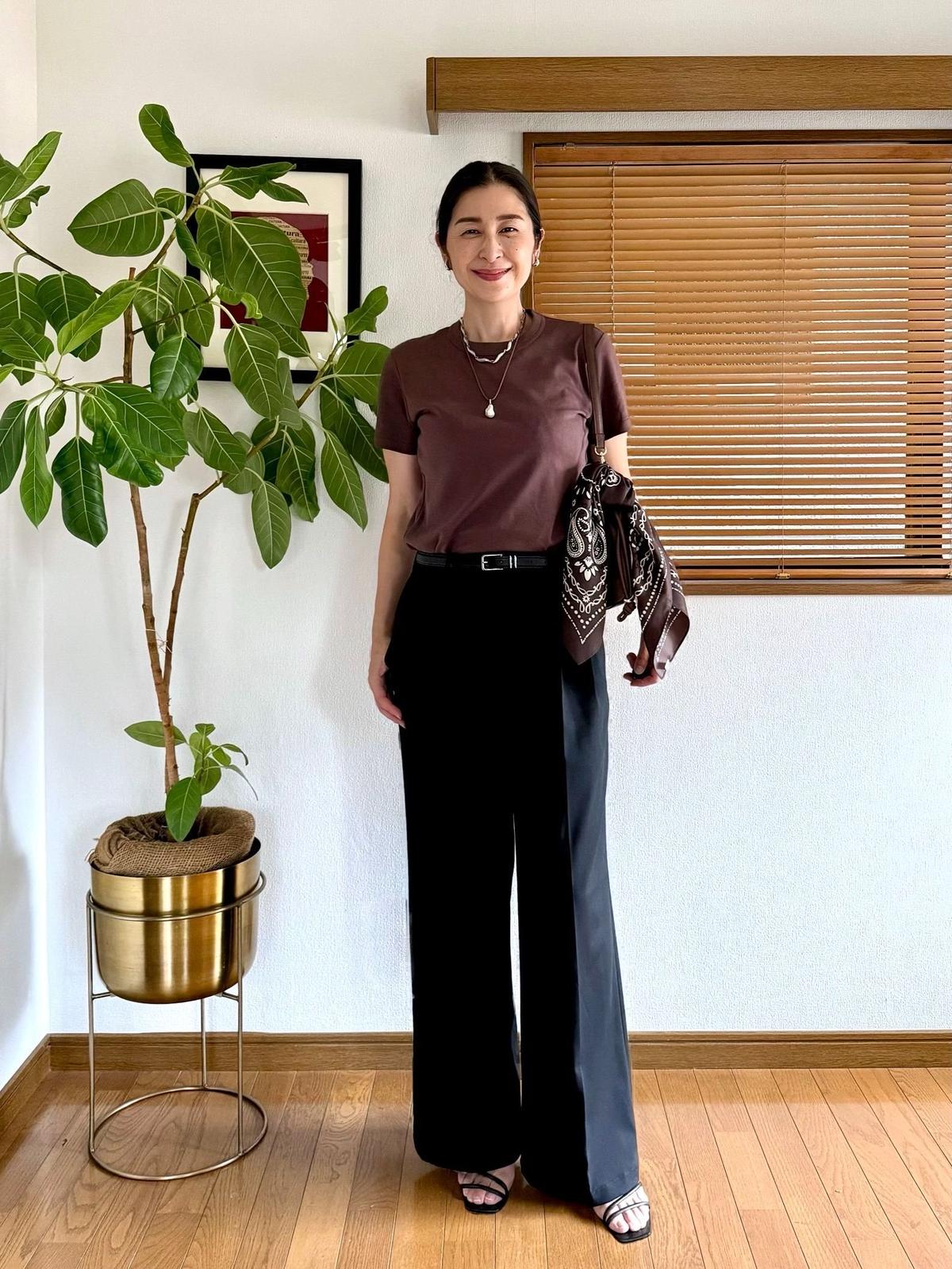 ユニクロスマートワイドストレートパンツ、UNIQLOブラウンTシャツに黒のパンツ、サンダルを合わせた女性。首にはネックレス、腰にはベルト。手首にバンダナを巻いている。背景には観葉植物と窓がある。