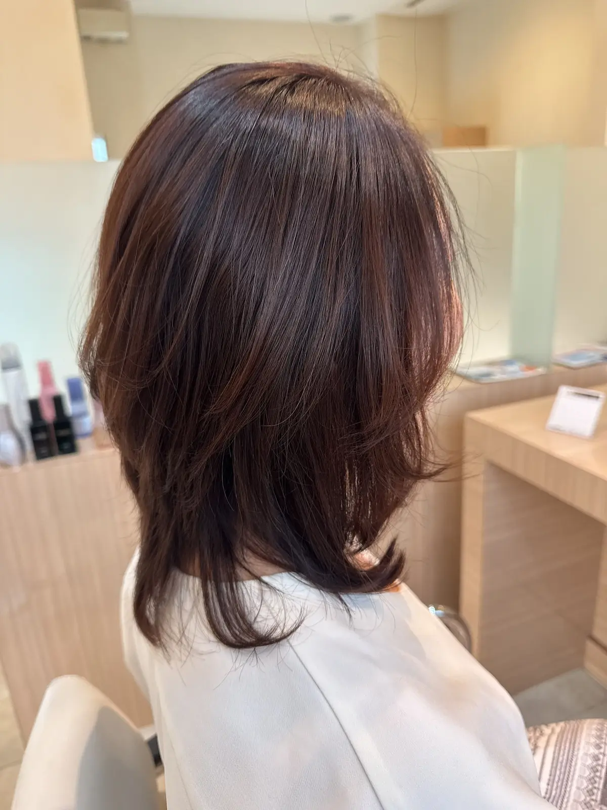 肩くらいの長さのダークブラウンのボブヘア。光沢があり、丸みを帯びたシルエット。背景には、美容室の家具や小物が写っている。