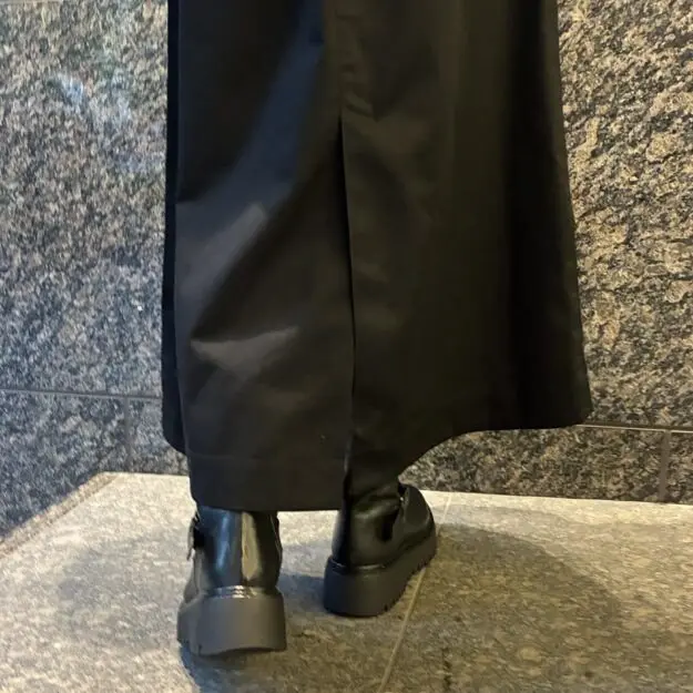 黒いワイドパンツと厚底ブーツの組み合わせ。パンツは裾が広がっており、ブーツは黒いレザー製で、太めのソールのデザイン。背景はグレーのタイル張りの床と壁。