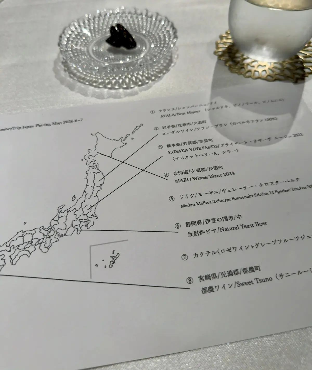 日本地図とワインのペアリングリストが記載された紙、クリスタル製のワイングラスに水と黒いワインチップが置かれている