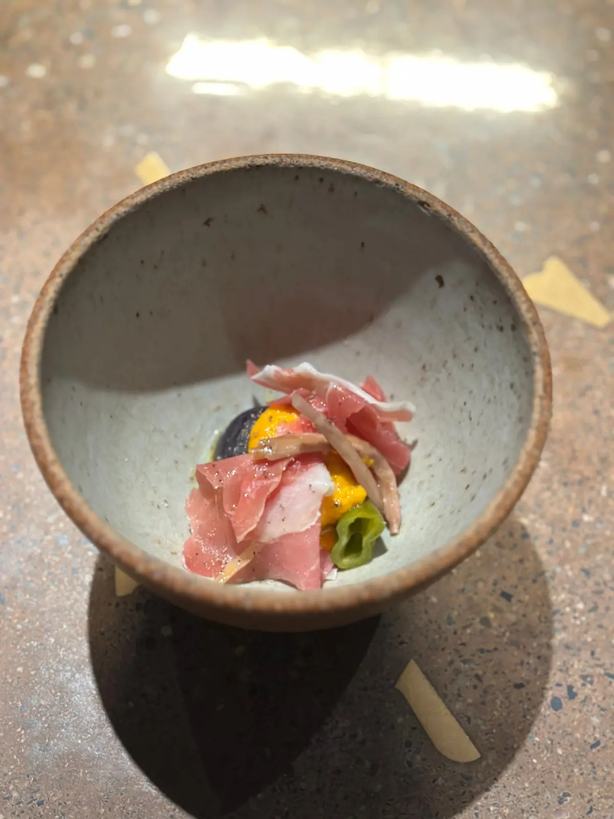 陶器の器に入った、ピンク色の薄切り肉、黄色いソース、緑色の野菜の盛り合わせ。