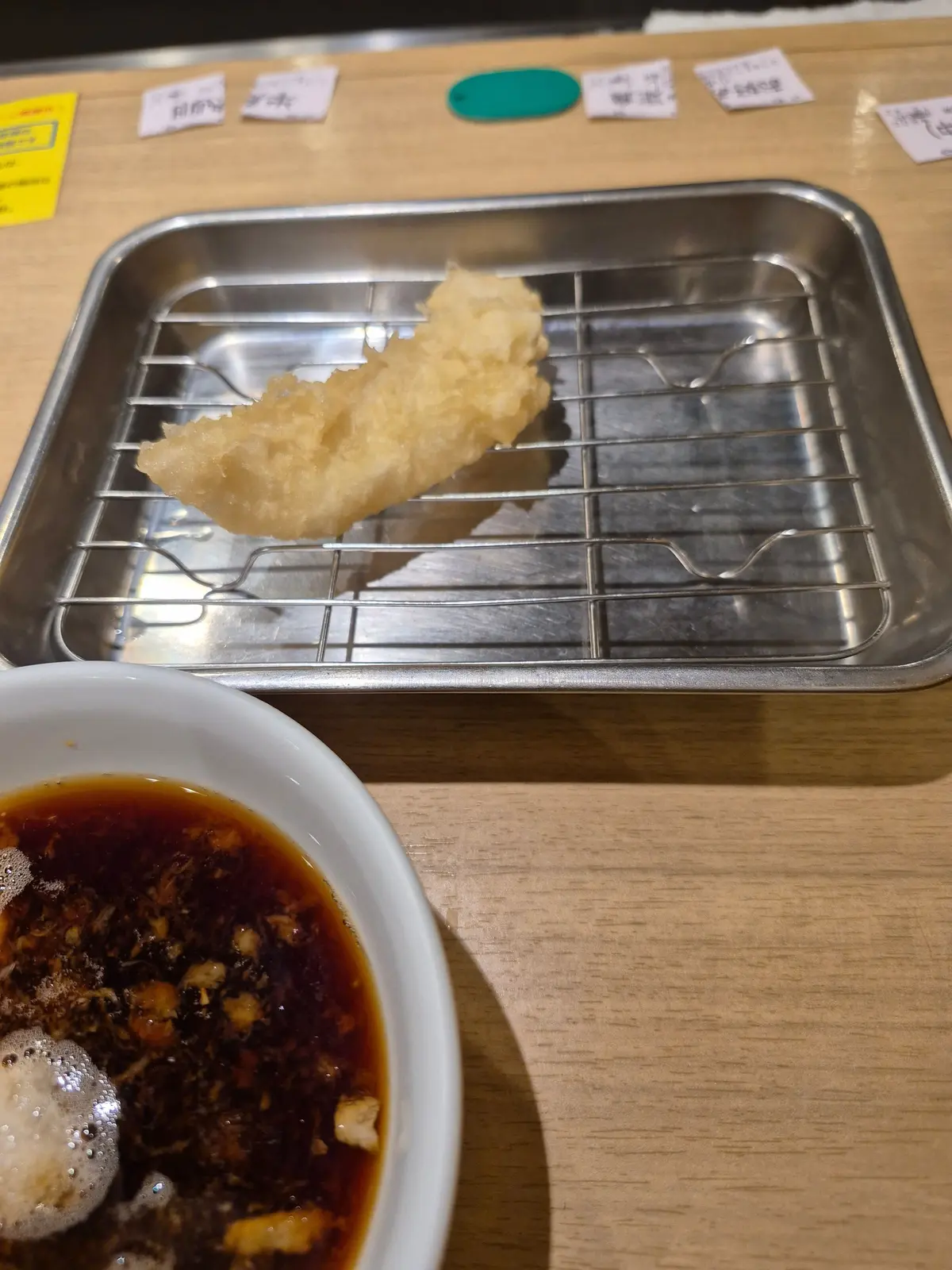 金属製のトレイに揚げ物が置かれ、その横には汁物が入った白い器がある。トレイは格子状で、揚げ物はクリーム色。汁物は濃い茶色。