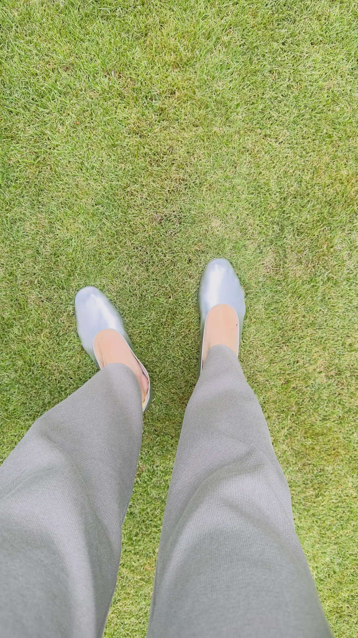 灰色のパンツとシルバーの靴を履いた足が、緑の芝生の上でまっすぐ前に向いている写真。